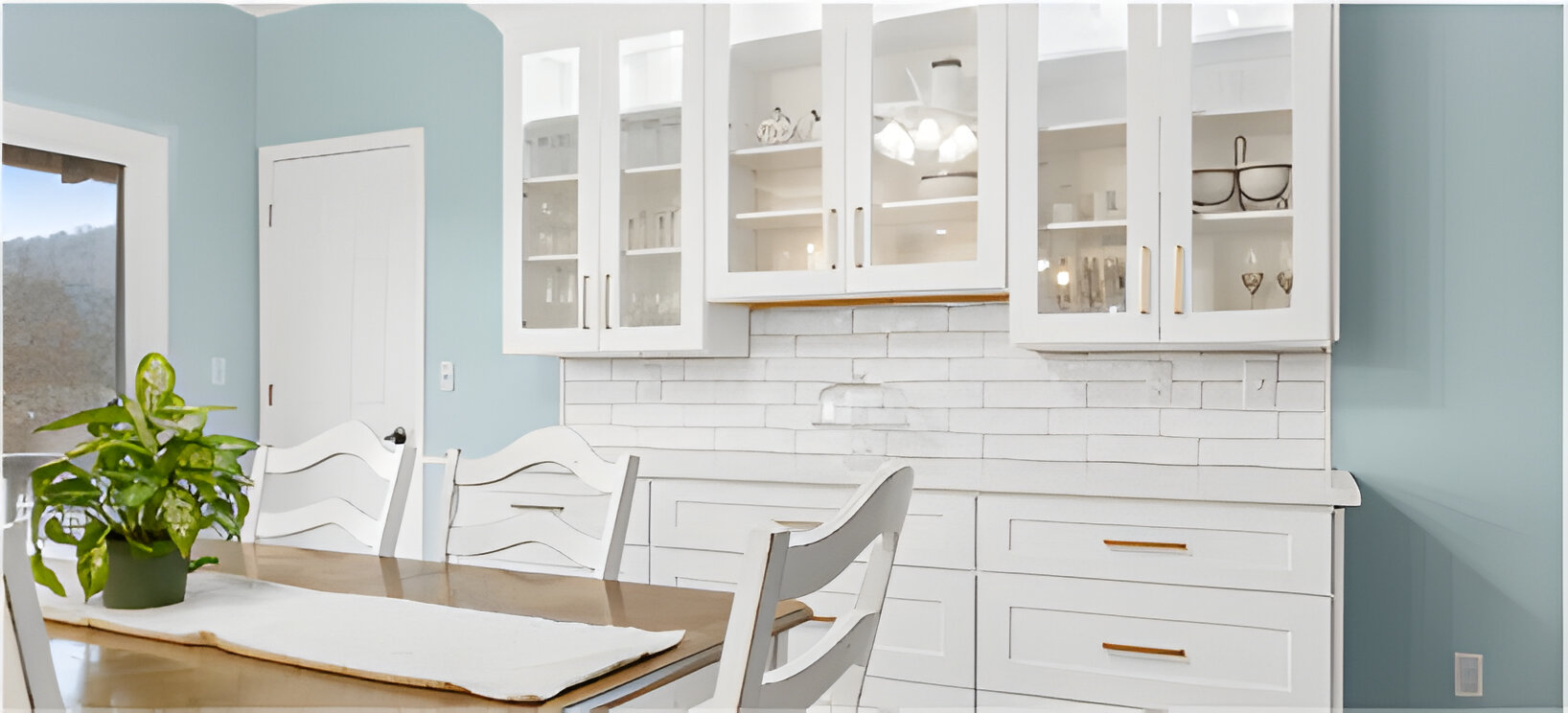 White bar cabinets with glass upper cabinets and drawer pull lower cabinets behind a charming farmhouse dining table