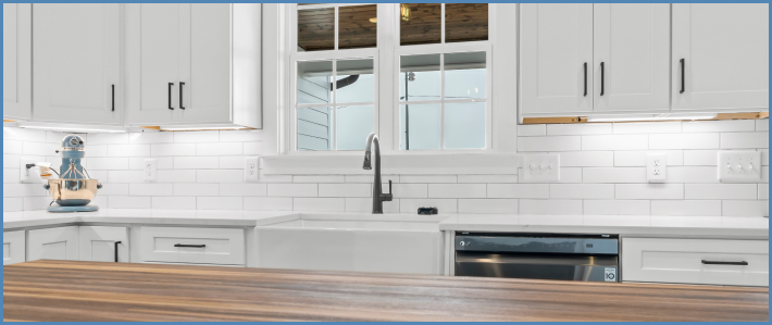Bright remodeled kitchen with white cabinets and counters, white subway tiling, a large basin sink, and an island with a wood countertop