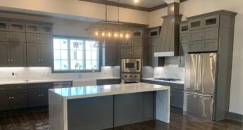 A modern kitchen renovated with slate gray cabinets, stainless steel appliances, and marbled waterfall island counter in white