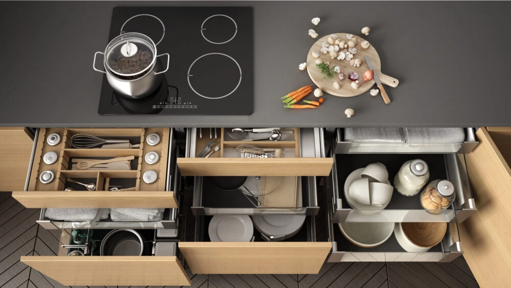 Top down view of a kitchen stovetop and counter with lower cabinet drawers and storage pulled open to reveal items organized with storage accessories