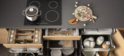 Top down view of a kitchen stovetop and counter with lower cabinet drawers and storage pulled open to reveal items organized with storage accessories