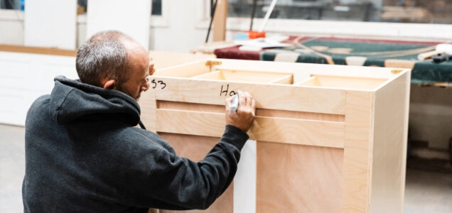 Cabinet builder writes notes on a set of partially constructed lower cabinets