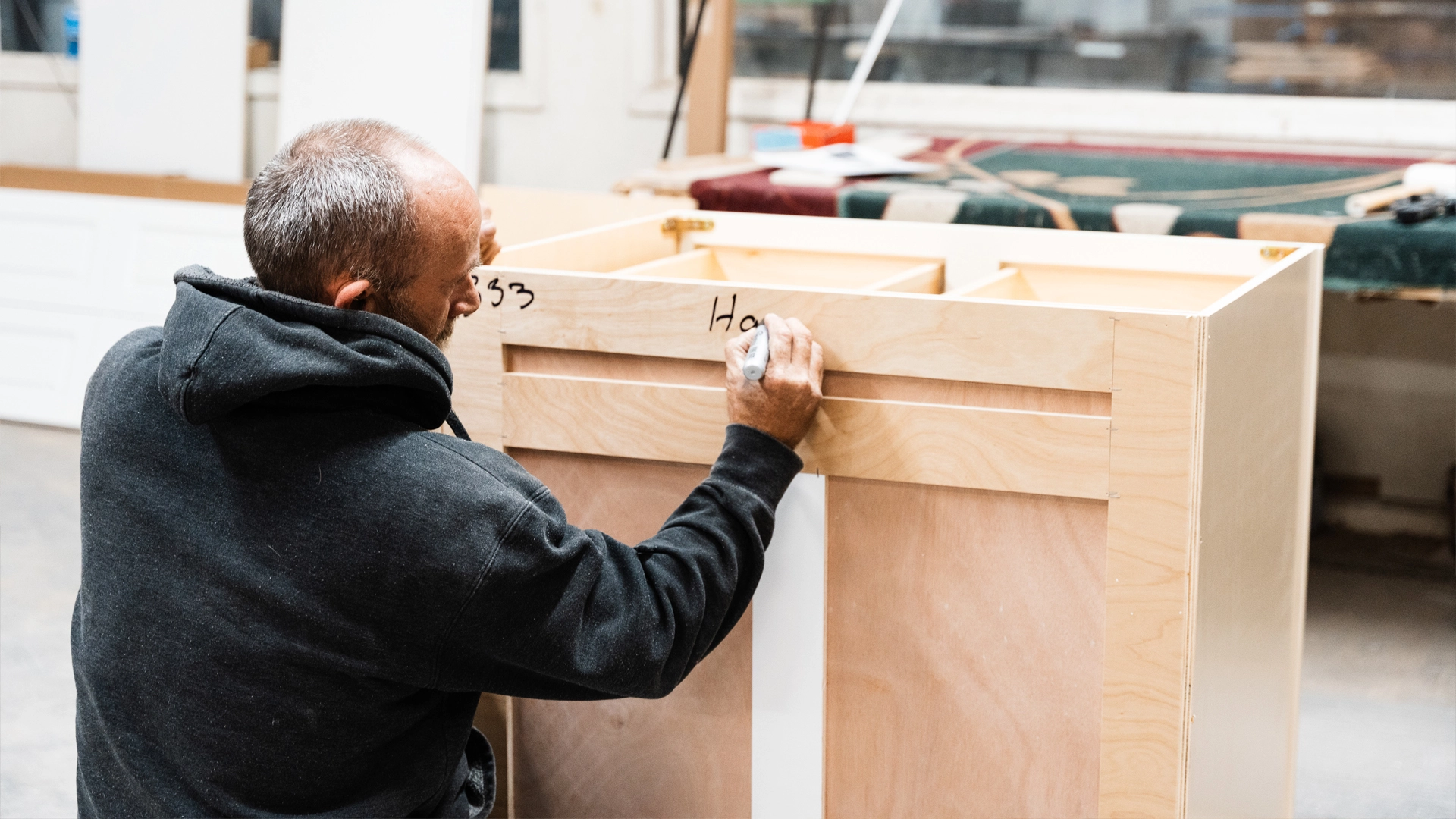 Cabinet builder writes notes on a set of partially constructed lower cabinets