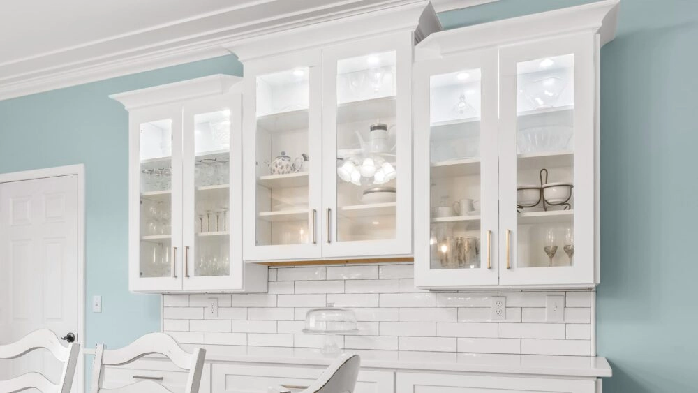 Trio of white upper cabinets with glass front doors and internal lighting