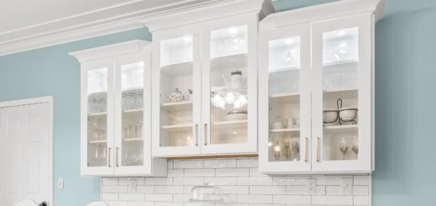 Trio of white upper cabinets with glass front doors and internal lighting