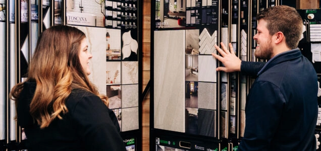 A Designery expert flips through sample countertop and backsplash materials with a customer in The Designery showroom