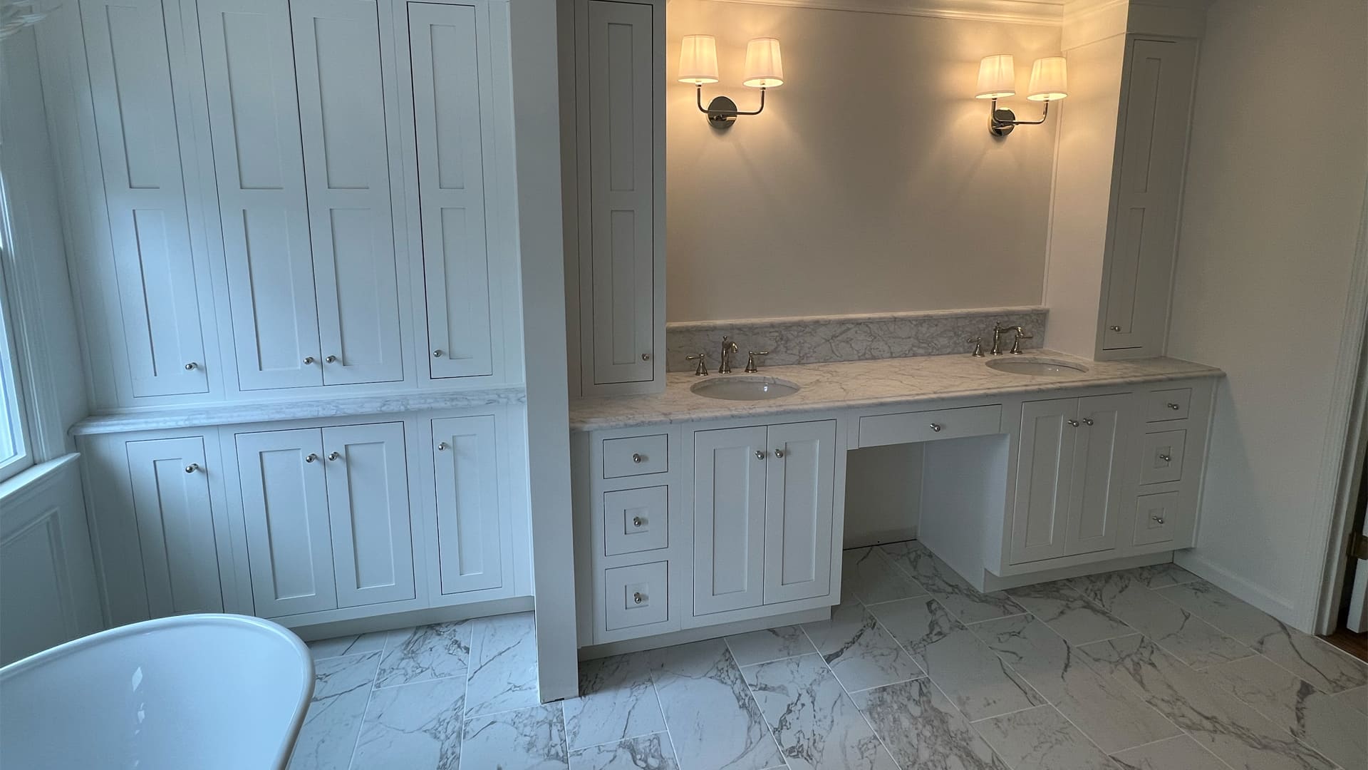 A relaxing all-white bathroom with marbled floor tiles, a double sink vanity with marbled counters, and a spacious built-in linen cabinet