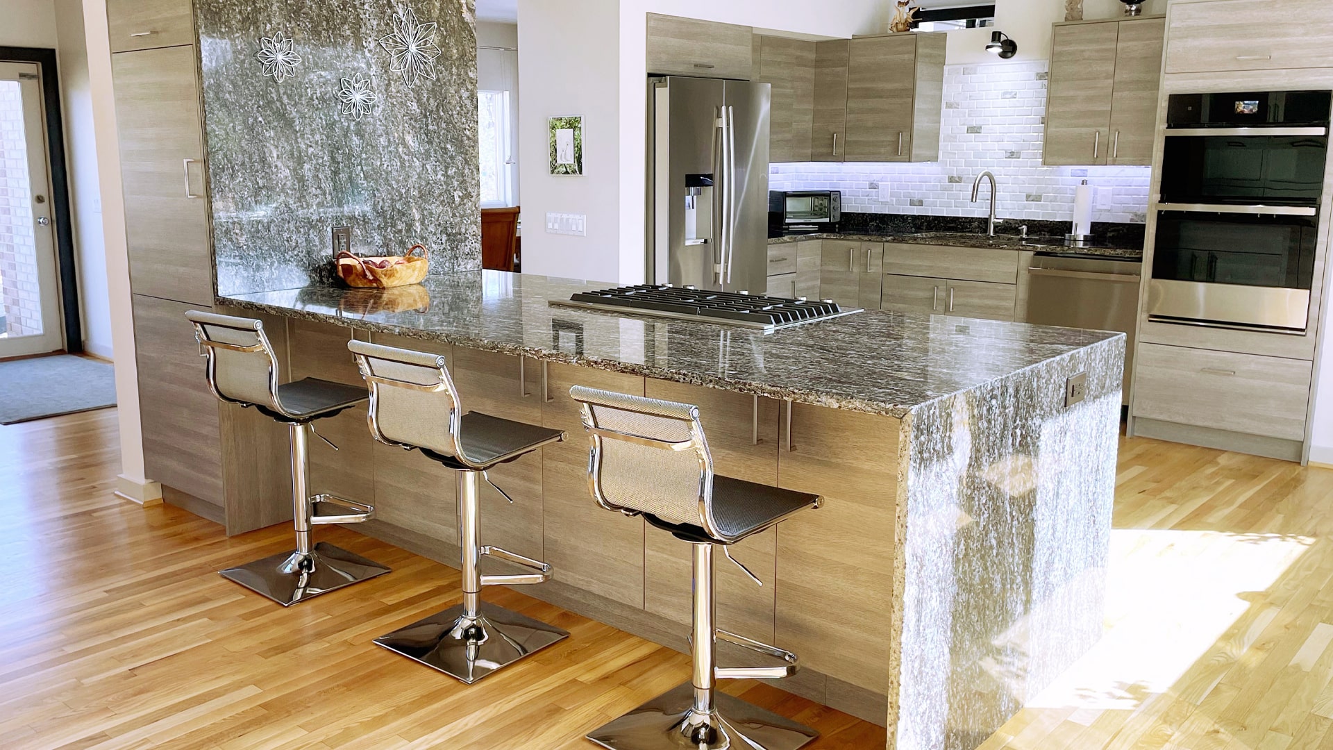 Contemporary kitchen remodel with a large, stone waterfall kitchen island with barstool seating