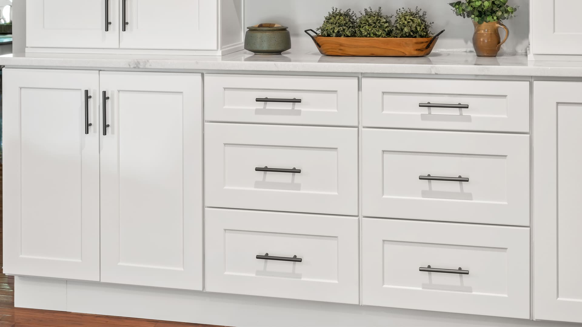 Close up of lower cabinets in white with shake doors and pull out drawers and a sleek, marbled white countertop
