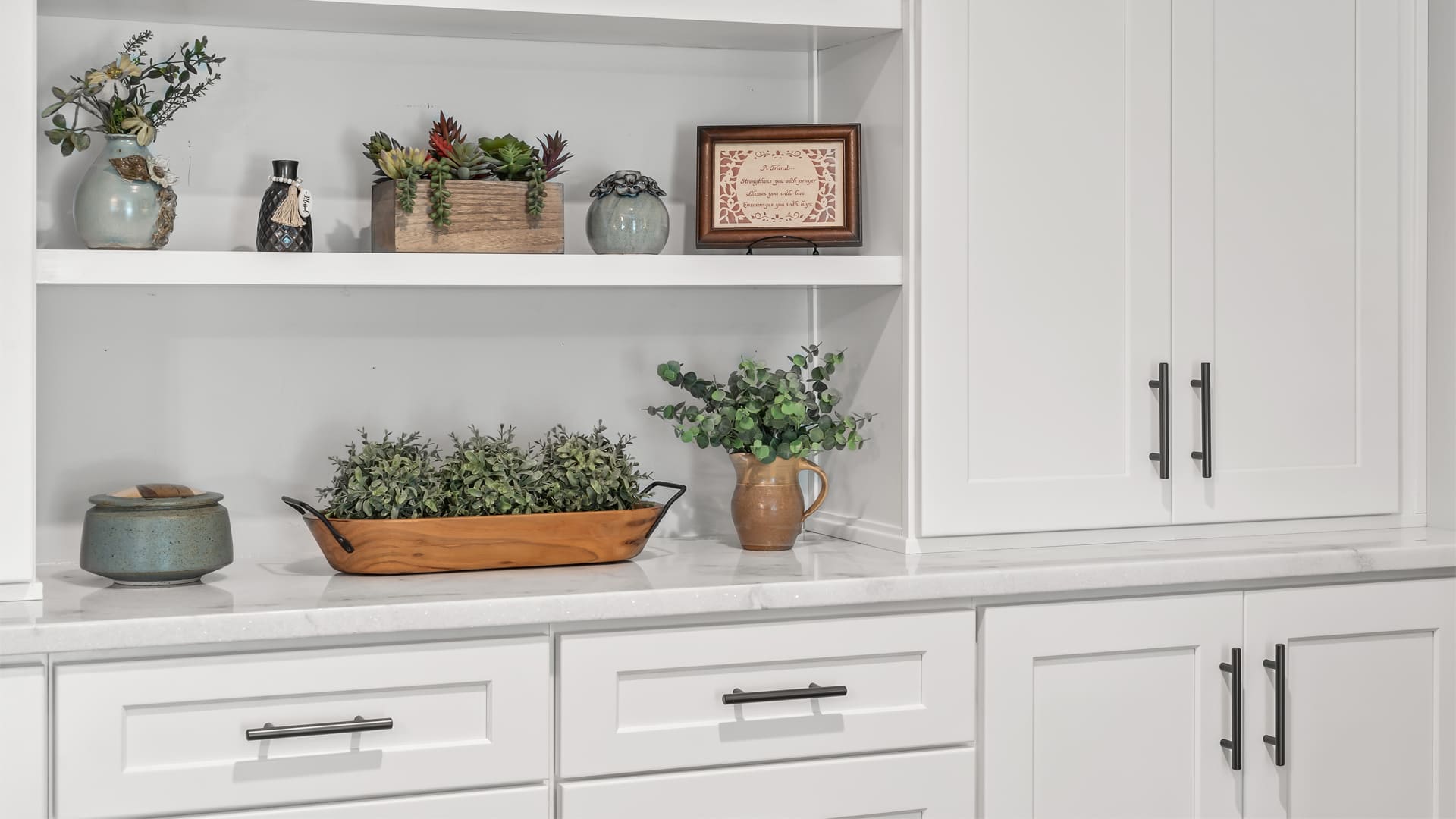Close up of built-in cabinet storage with all-white shaker doors and drawers as well as upper open shelving for plants and decor