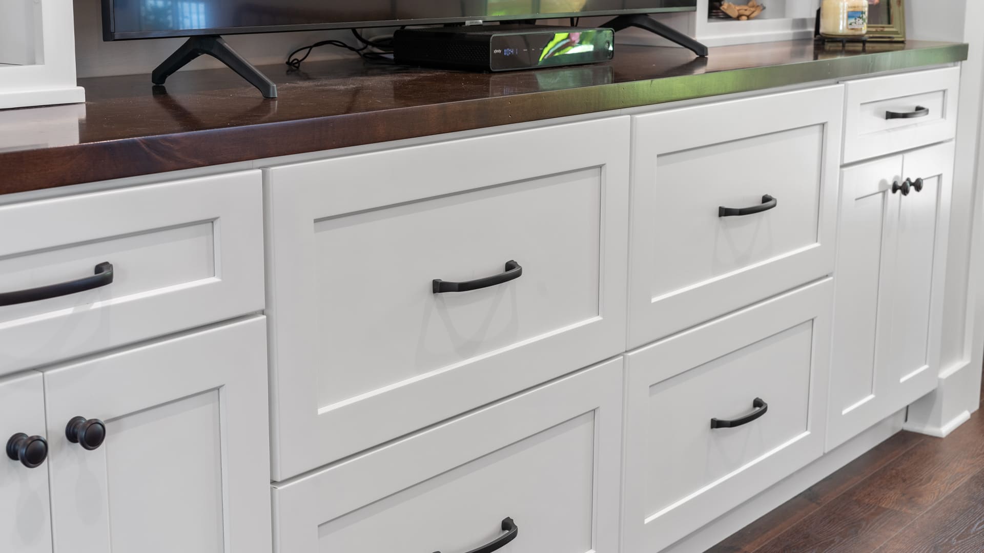 Close up of a built-in cabinet entertainment center with white shaker cabinet doors and drawer and a sleek dark wood countertop