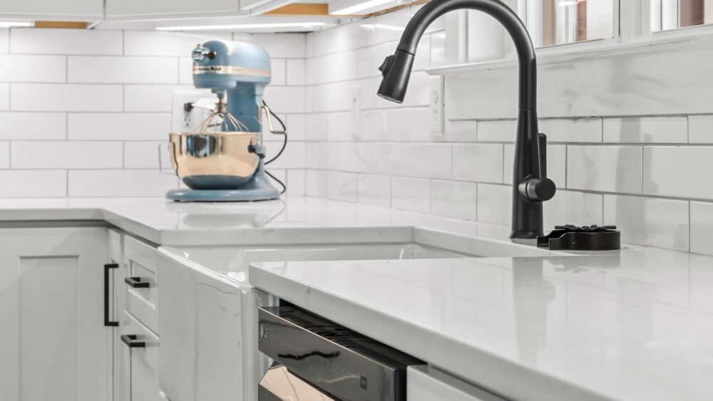 Close up of a white, marbled kitchen countertop and basin sink with a black, pullout spray kitchen faucet