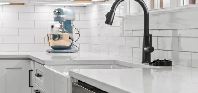 Close up of a white, marbled kitchen countertop and basin sink with a black, pullout spray kitchen faucet