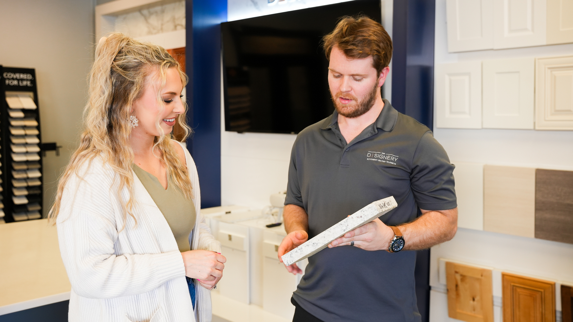 A Designery expert shows a customer a piece of sample countertop in The Designery showroom