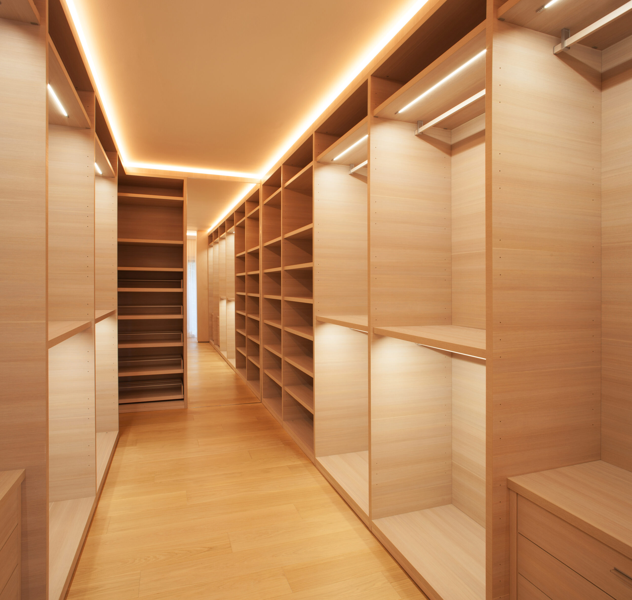 Expansive hallway walk-in closet with rows of sleek open storage, clothes hanging space, pull-out storage, and modern bar lighting in the cabinetry