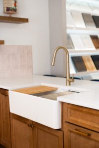 A stylish kitchen sink area featuring a white farmhouse sink, a brass high-arc faucet, and warm wooden cabinetry with brass handles. The white quartz countertop contrasts beautifully with the rich wood tones.